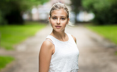 Beautiful portrait of a blond girl looking at the camera. She is wearing a white dress, has her...