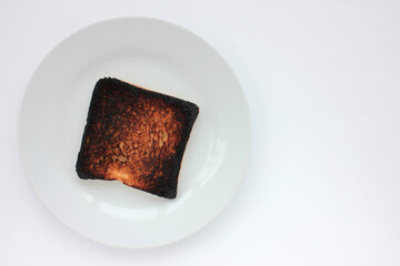 Piece of burnt toast bread on a plate on a white background. Top view, copy space