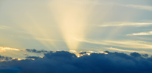 Fototapeta na wymiar Yellow sunrays shining over clouds with blue sky