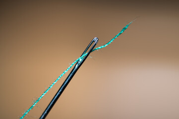 Close up of the eye of a needle with teal thread going through it, orange background