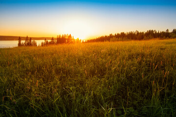 Panoramic view of the Kama River from the hill, green meadow, rural road, sunset sky and sun rays.