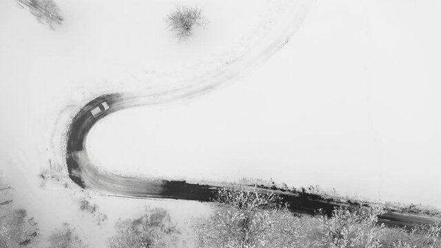 Cars driving on winter country road in snowy forest, aerial view from drone. Aerial view of car driving in a wavy and icy road 