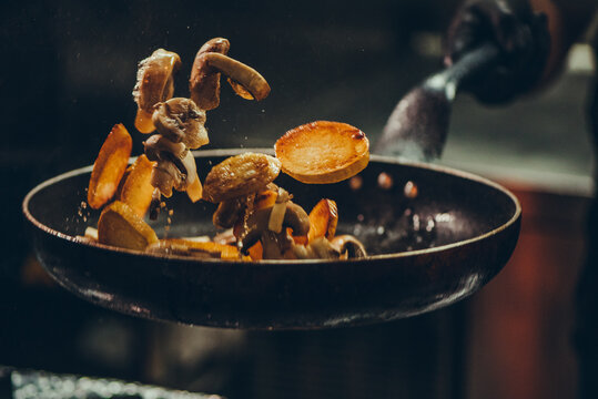 Chef at work. Hand holds a hot pan with fried vegetables 