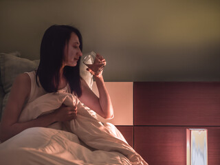 Young woman in bed, drinking a glass of water before going to sleep.