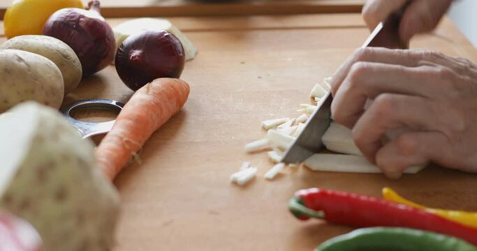 Vegetable soup preparing, chopping celery root at cutting board using sharp knife, close up