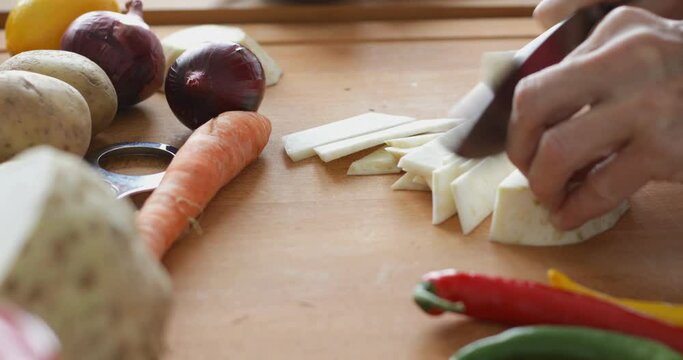 Vegetable soup preparing, chopping celery root at cutting board using sharp knife, close up