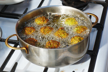 A saucepan on a gas stove in which meatballs are boiled in boiling oil.