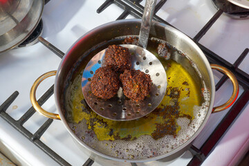 Three meatballs are taken out of the pan with boiling oil with a slotted spoon.