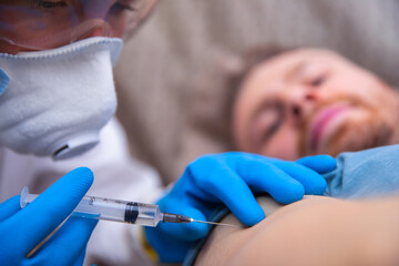 medicine, vaccination and healthcare concept - doctor wearing face protective medical mask for protection from virus disease with syringe doing injection of vaccine to male patient.