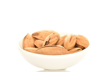 Dried unpeeled almonds in a white ceramic saucer, close-up, isolated on white.