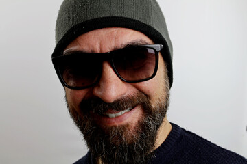 Close-up handsome smiling bearded man with sunglasses and wool cap on his head