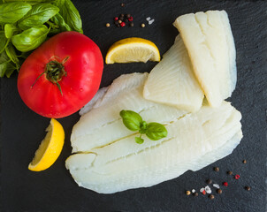 Raw halibut fish fillet, tomato, lemon basil and spices on black stone board, top view - 410474572