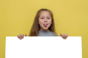 Place for your advertisement. Baby girl pointing to blank white billboard on yellow background, copy space. Emotions