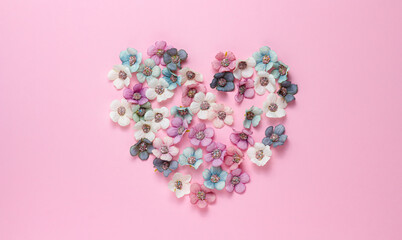 Heart shape of white, blue and pink flowers on a pink background. Valentine's Day, love, congratulations. Pastel colors. Top view