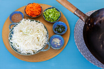 Top view of cooking ingredients in bowls and plates. Cabbage, carrot, chili peppers, garlic, mustard seeds at blue background.