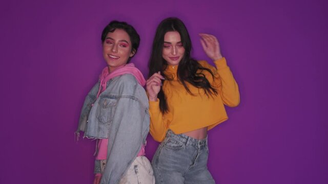 Two happy pretty stylish cool diverse gen z zoomers teen girls bloggers having fun dancing together on purple background shooting social media video, recording content for online channel.