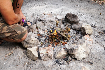 a man in a hat fanning a bonfire in nature