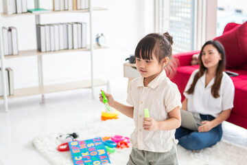 Cute girl standing in bedroom by the bed at home and blowing soap bubbles. Adorable girl blowing soap bubbles in bedroom. Young women at home with little girl are having fun and blowing soap bubbles.