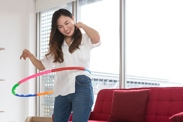 Happy Asian women playing Hula Hoop in the living room at home. Young adult woman learning to play with a hula-hoop in a living room. © Avirut S.