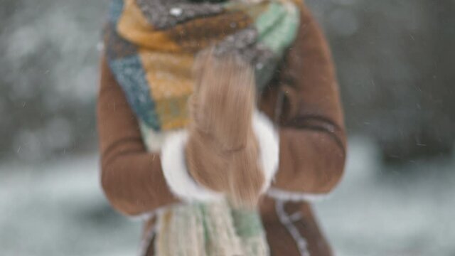 Closeup on female in brown hat and scarf outside in the city park in winter in sheepskin coat cleaning snowy mittens.
