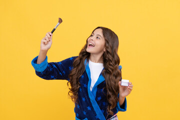 happy kid girl in sleepwear using cosmetic brush and powder foundation, skin care