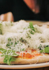 Vista detallada de una pizza de carnes con rúgula y mucho queso parmesano puesto perfectamente por encima.