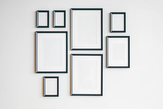 Multiple many black picture frames on white wall. Woman hanging a frame on a wall.