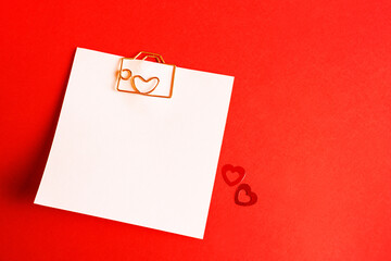 Square sheet for notes with a paper clip in shape of a letter and a heart. Decor of couples in love with hearts on a red background. Valentine's Day, message, greeting, declaration of love. Copy space