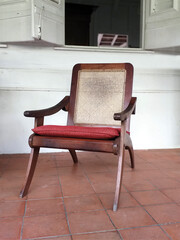 Classic antique wooden chair with mesh backrest and red cushion. Front view of colonial solid wood armchair on porch of tropical house. Rustic atmosphere of the FWI. Vintage furniture and decoration.
