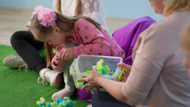 child with disabilities spends time with teacher sitting on beanbag chairs, little girl with down syndrome plays with tactile toys