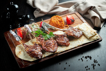 Lamb rack cooked on the grill with pita bread, bulgur and grilled vegetables on a wooden board. Turkish shashlik. Close up, selective focus