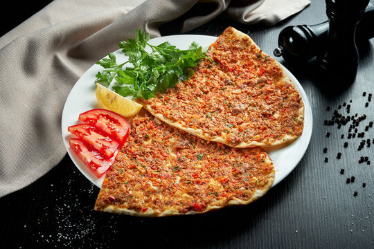 Lahmacun is a popular Turkish dish. Thin crispy tortilla with minced lamb, tomatoes and bell pepper on black background