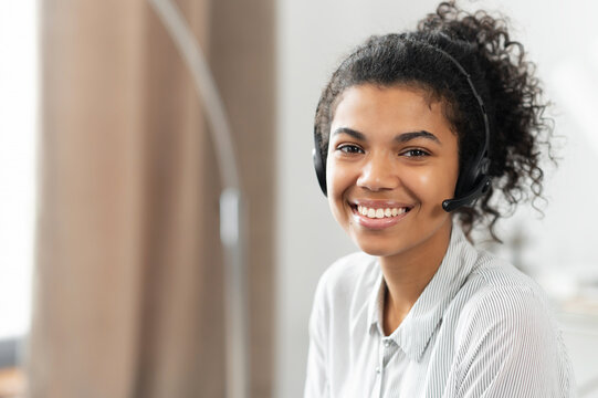 Headshot of friendly charming African American mixed-race woman in headset, smiling at camera working in the customer service department as call center operator, providing consultations on the phone