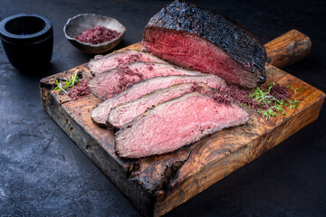 Traditional Commonwealth Sunday roast with sliced cold cuts roast beef with herbs and salt served as close-up on an old rustic wooden board