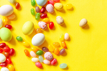 Happy Easter concept. Preparation for holiday. Easter candy chocolate eggs and jellybean sweets isolated on trendy yellow background. Simple minimalism flat lay top view copy space.