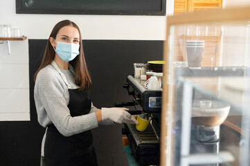 Fototapeta na wymiar Female barista wearing medical mask preparing coffee take away in a cafe, professional coffee brewing. Small business works during outbreak