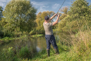 Fisherman holding a fishing rod by the river. Summer sunny day