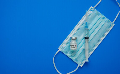 Transparent medical ampoules, syringe and protective mask on a light blue background. Protection during a pandemic.