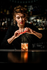 beautiful female bartender gently sprinkles on glass with cold alcoholic cocktail on the bar counter