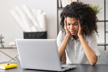 Exhausted millennial African American female office worker touching temples, does not understand...