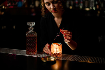 female bartender neatly decorates glass of cold alcoholic cocktail with olive