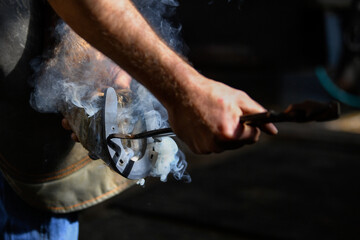 Farrier hot shoeing a horse - adjusting a hot horseshoe to the hoof