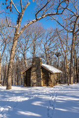 Fototapeta na wymiar Log cabin in the snow covered woods with blue skies behind.