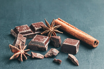 Chopped chocolate cubes, cinnamon stick and star anise on dark background with copy space, close-up view