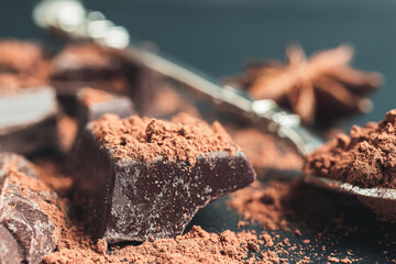 Chocolate chunk, chopped chocolate cubes with cocoa powder on dark background, close-up view