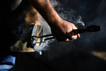 Farrier hot shoeing a horse - adjusting a hot horseshoe to the hoof