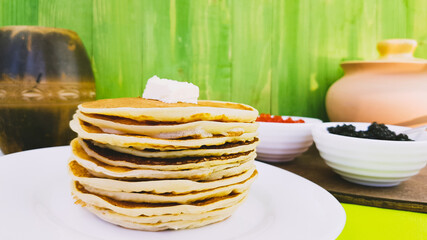 pancakes on a white plate. on the pancakes - a piece of butter. black sturgeon and red salmon caviar are served with pancakes on Shrovetide