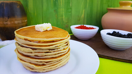 pancakes on a white plate. on the pancakes - a piece of butter. black sturgeon and red salmon caviar are served with pancakes on Shrovetide