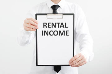 Rental income inscription on a tablet in the hands of a businessman on a gray isolated background.