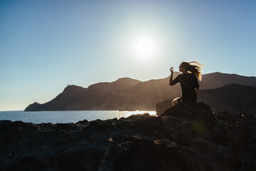 Person sitting on cliff at the ocean with wind in the hair